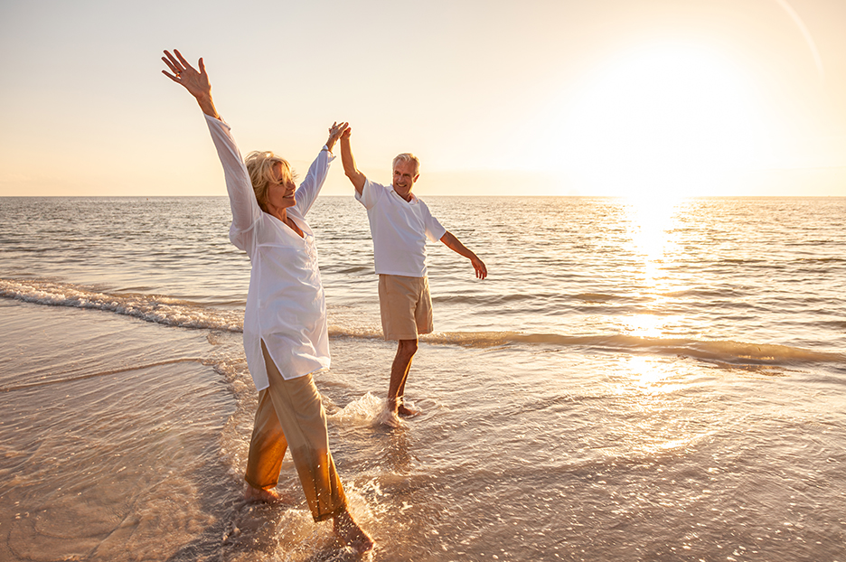 Happy Senior Old Retired Couple Walking Holding Hands on Beach a